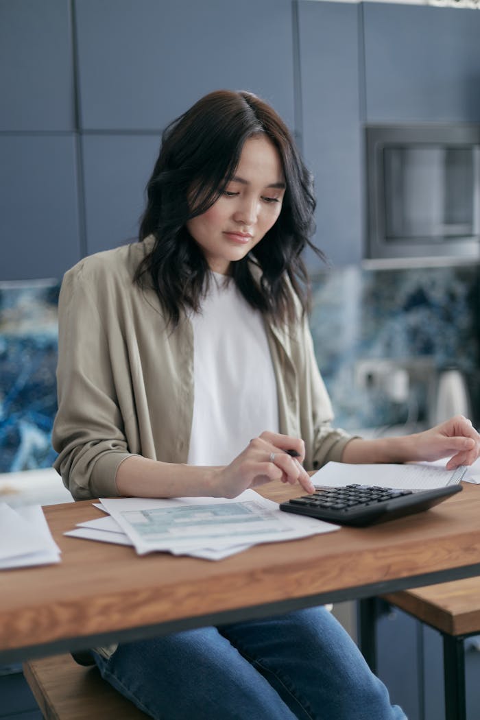 Focused woman calculating budget at home with calculator and papers, promoting financial planning.